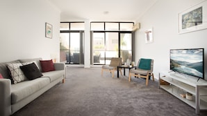 A modern living room with a grey sofa, a TV, and a dining area with chairs and a table. - Chic Unit With Rooftop Terrace Near Sights & Shops (Sydney)