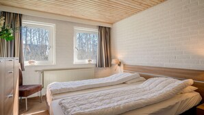 Une chambre avec deux lits, un plafond en bois, un mur en briques, un radiateur et une fenêtre avec des rideaux.