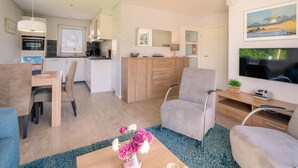 Un salon moderne comprenant un canapé, une table basse agrémentée de fleurs, un téléviseur et un coin cuisine avec une table à manger et des chaises.