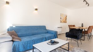 Ein modernes Wohnzimmer mit einem blauen Sofa, einem Couchtisch, einem Essbereich mit Tisch und Stühlen sowie einem Bild an der Wand.