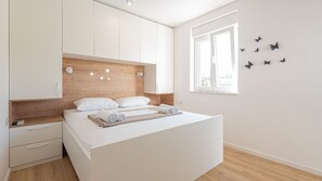 Ein modernes Schlafzimmer mit Bett, weißem Kleiderschrank, Holz-Kopfteil und einem Fenster mit Schmetterlingen.