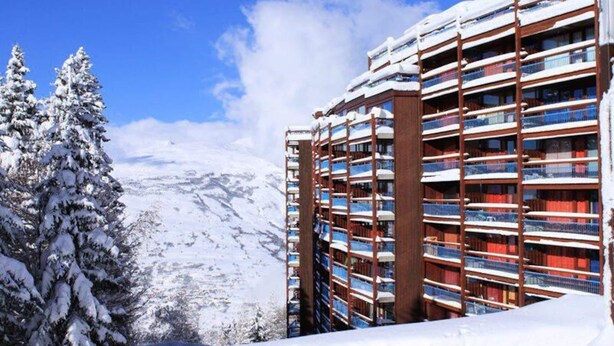Un hotel de varios pisos con balcones, con una imponente montaña nevada de fondo.