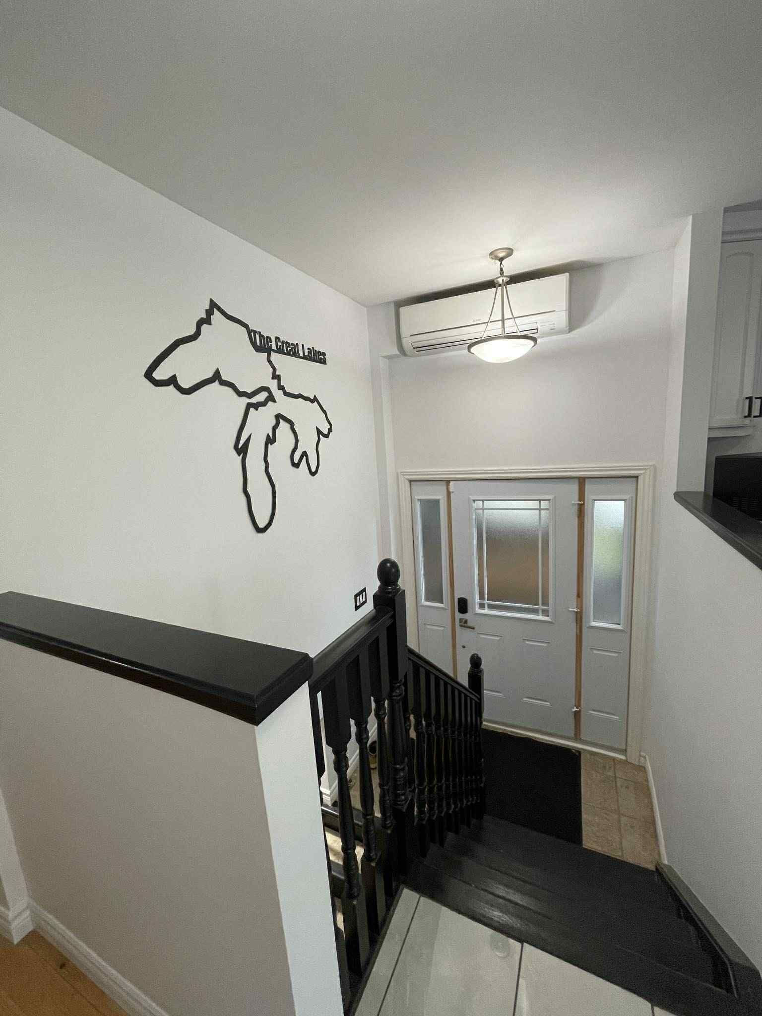 Un escalier avec une rampe noire, un mur blanc orné d’une carte et une porte dont les panneaux sont en verre dépoli.