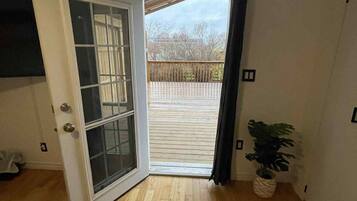 Une pièce avec un plancher en bois, un lit recouvert d’une couvre-lit à motifs floraux, une porte-fenêtre coulissante donnant sur une terrasse extérieure et une plante en pot.
