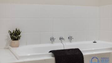 Une salle de bain avec une baignoire blanche, deux robinets et une plante en pot.