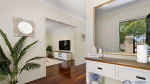A modern living room with a wooden floor, a large mirror, a television, and a welcome sign. - 3 bedroom Villa walking distance to Mandurah foreshore (Mandurah)