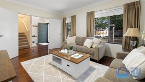 A spacious living room with a beige sofa, a wooden coffee table, and a view of the outdoors through large windows. - 3 bedroom Villa walking distance to Mandurah foreshore (Mandurah)