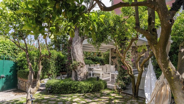 Een tuin met een pergola, een zithoek en een pad van stenen.