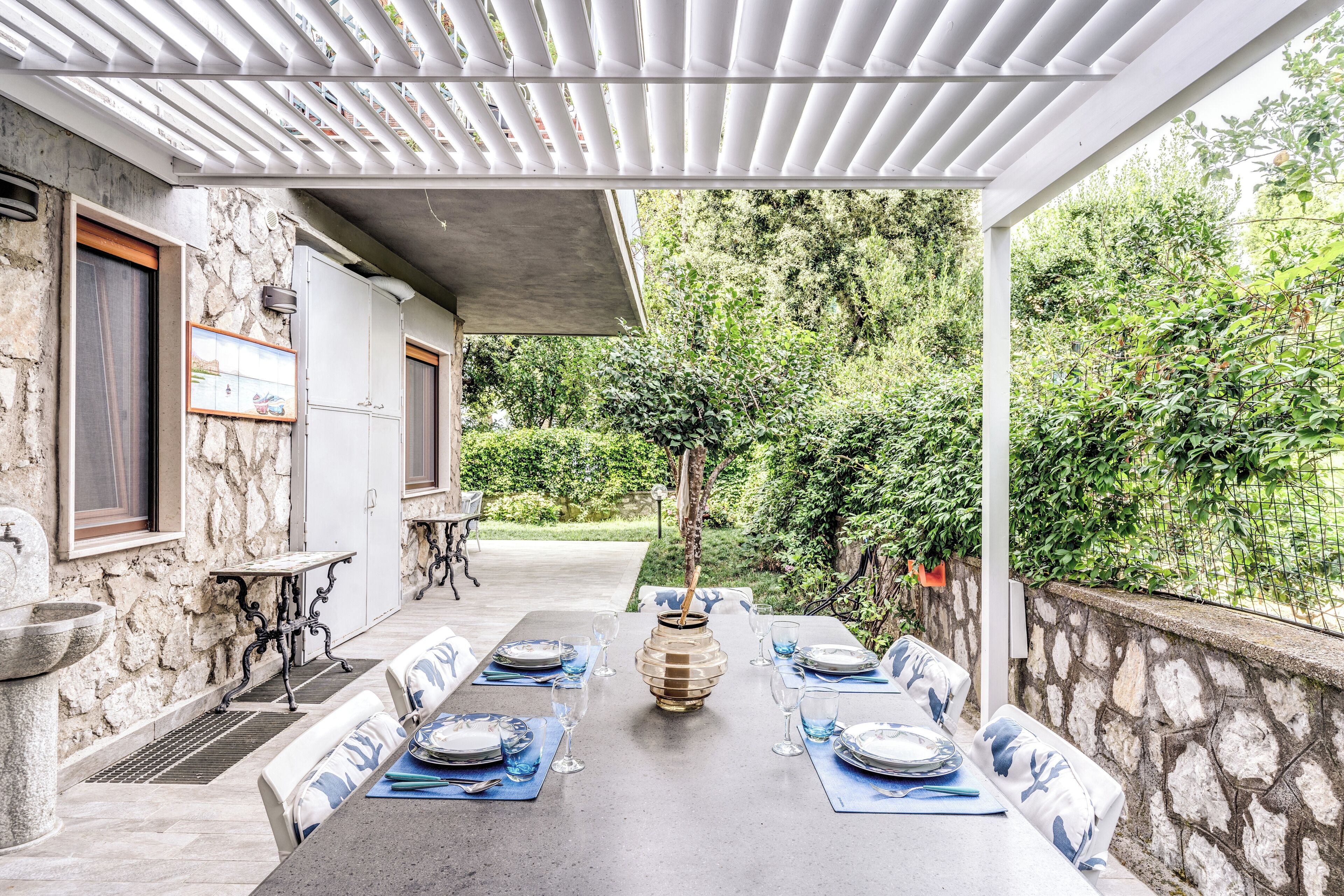 An outdoor dining area with a stone wall, a pergola, and a table set for four.