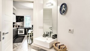 Een moderne keuken met witte kasten, een fornuis en een gootsteen. Er is een eethoek met een tafel en stoelen. Een grote spiegel en een decoratief bord hangen aan de muur.