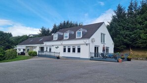 A white two-story building with a grey roof, a covered porch, and a fenced driveway. - Lochbroom Lodge (Ullapool)