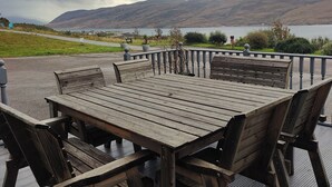 A wooden deck with a table and chairs, overlooking a lake and hills. - Lochbroom Lodge (Ullapool)