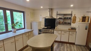A kitchen with a central island, a stove, a refrigerator, and a window with a plant. - Lochbroom Lodge (Ullapool)