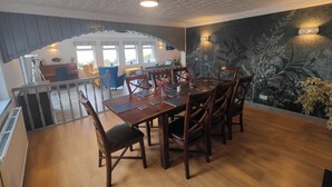 A dining area with a wooden table and chairs, a kitchen in the background, and a decorative wall with a plant mural. - Lochbroom Lodge (Ullapool)