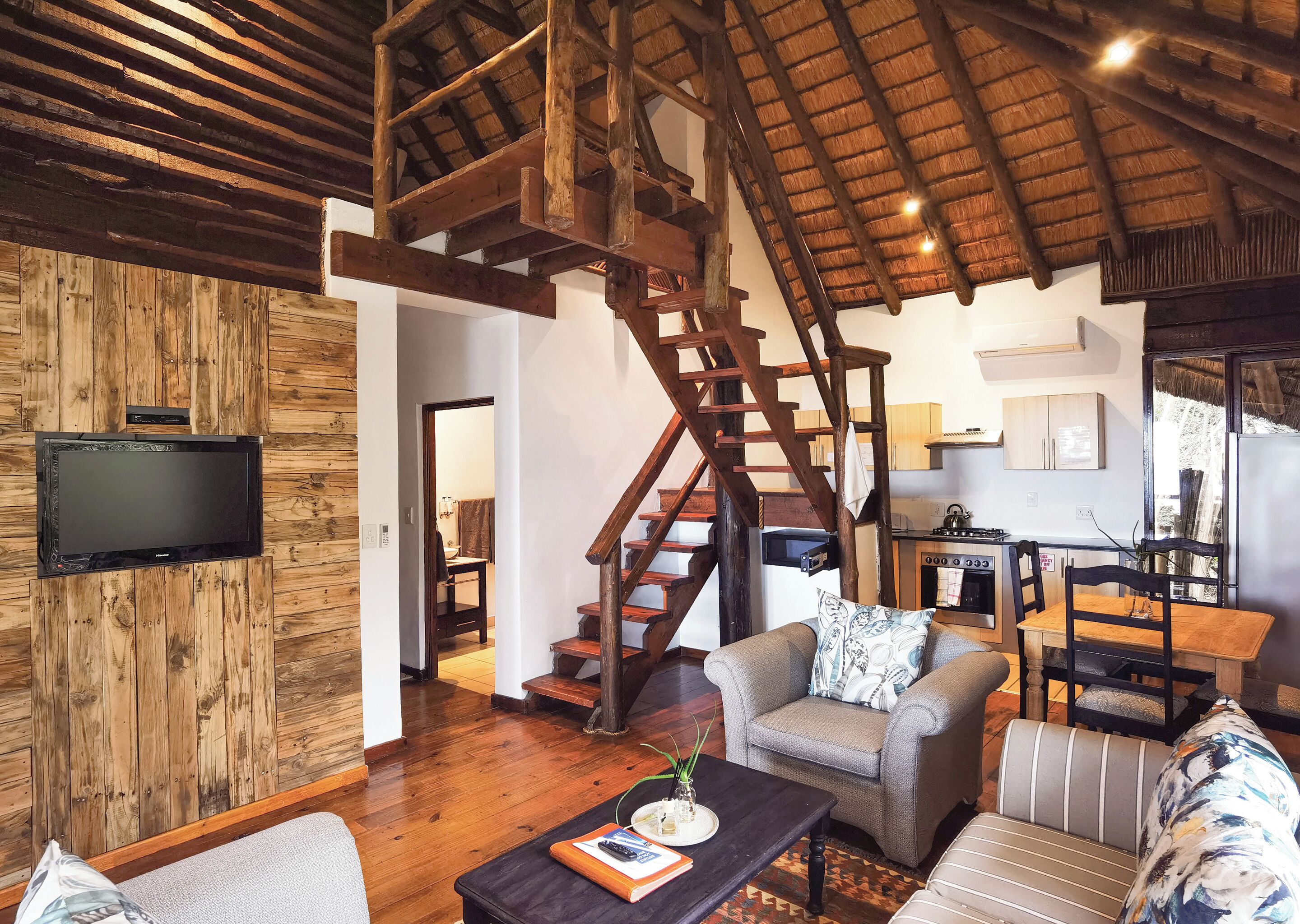 Un vaste espace de vie doté d’un plafond en bois, d’un escalier, d’une cuisine et d’un téléviseur à écran plat fixé à un mur en bois.
