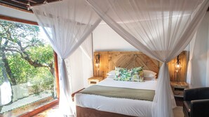 A bedroom with a wooden headboard, a bed with white bedding, a nightstand, a bedside lamp, and a view of greenery outside. - Sobhengu Lodge by Dream Resorts (KwaNibela)