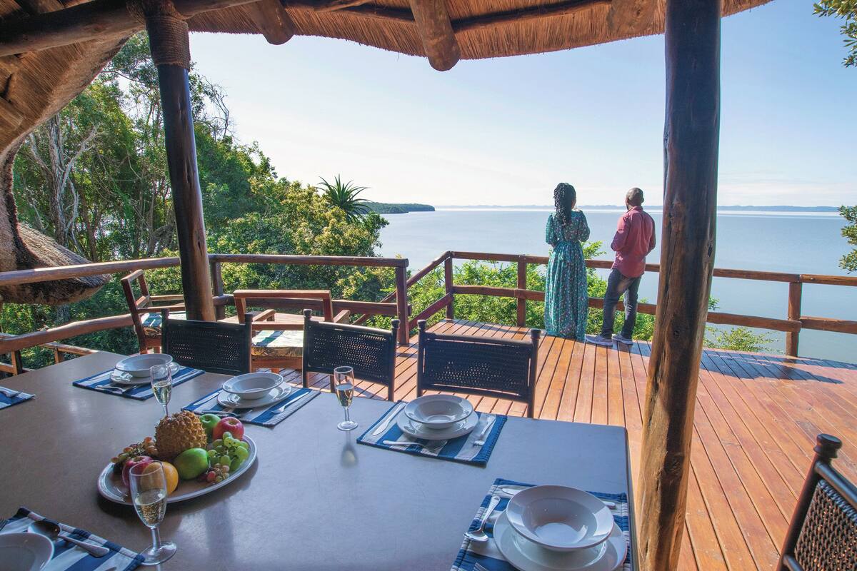 Um deck de madeira com uma mesa posta para dois, com vista para um corpo de água.
