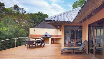 Una terraza de madera con comedor, una parrilla y una silla de descanso.