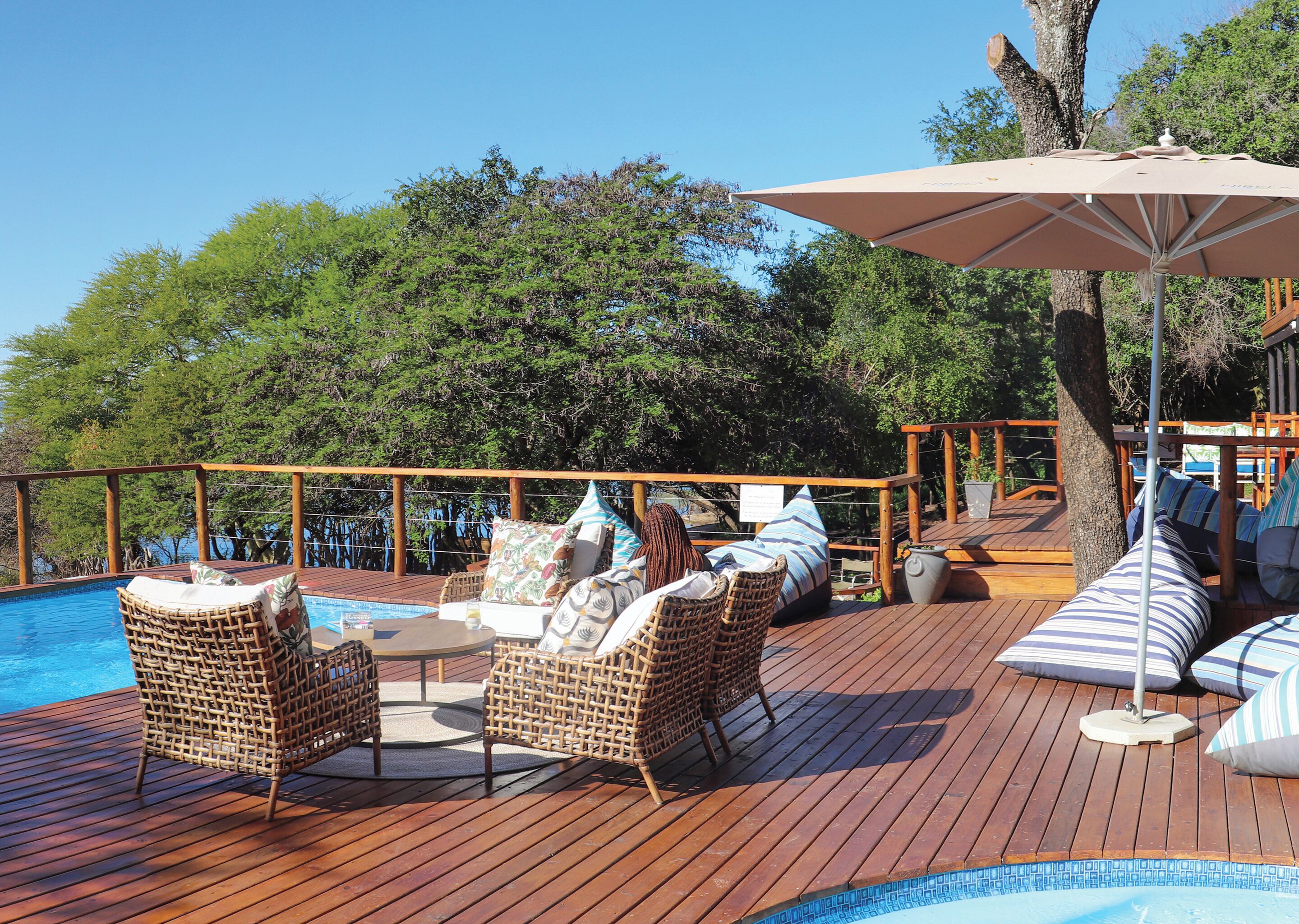 Une terrasse en bois avec des meubles en osier, une piscine et un grand parasol.