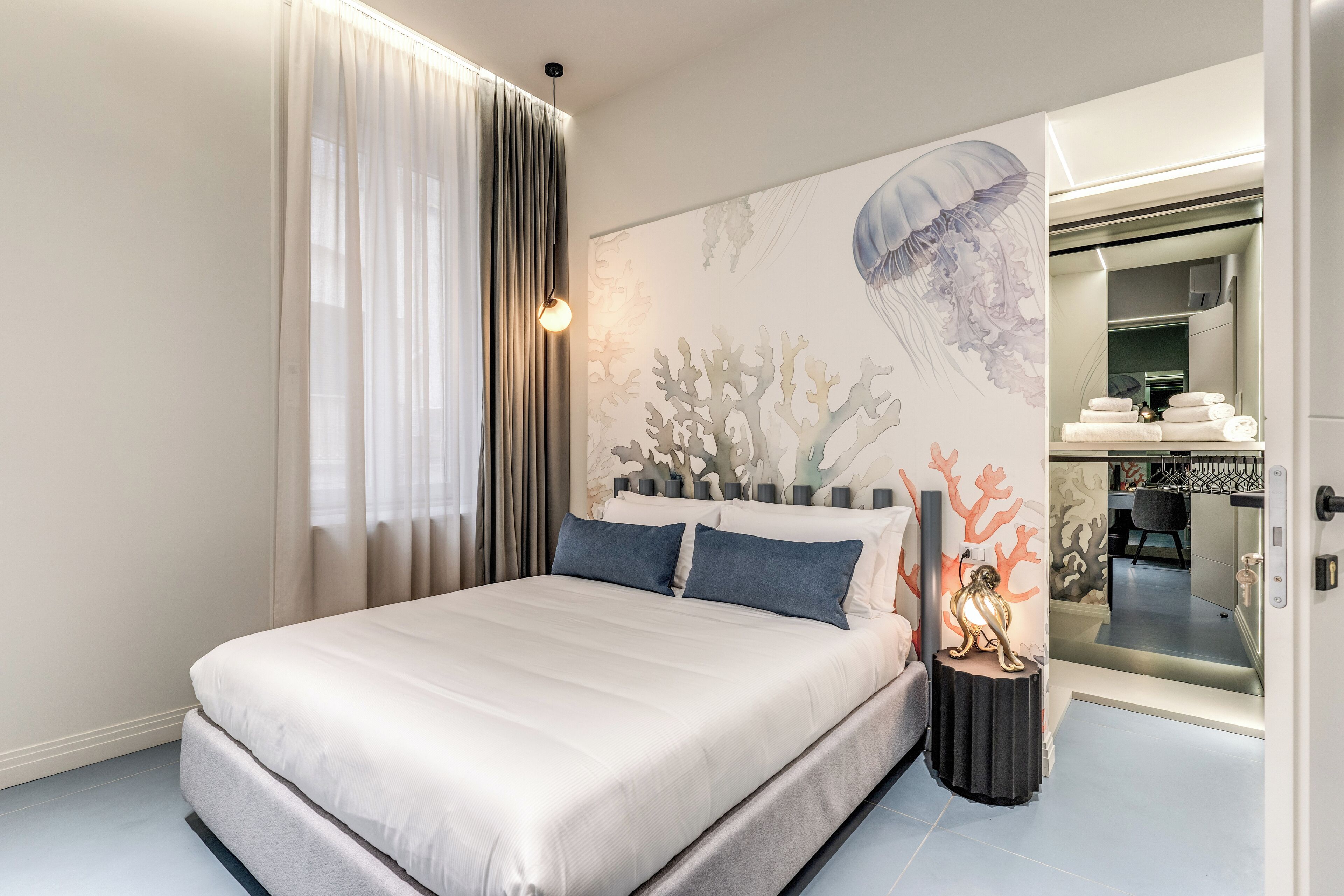 A modern bedroom with a large bed, a wall mural, and a bathroom visible through an open door.