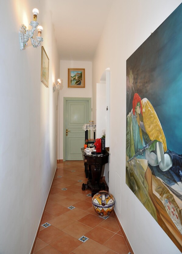 Ein Flur mit gefliestem Boden, einer grünen Tür, einem Tisch mit einer Vase und einem großen Gemälde an der Wand.