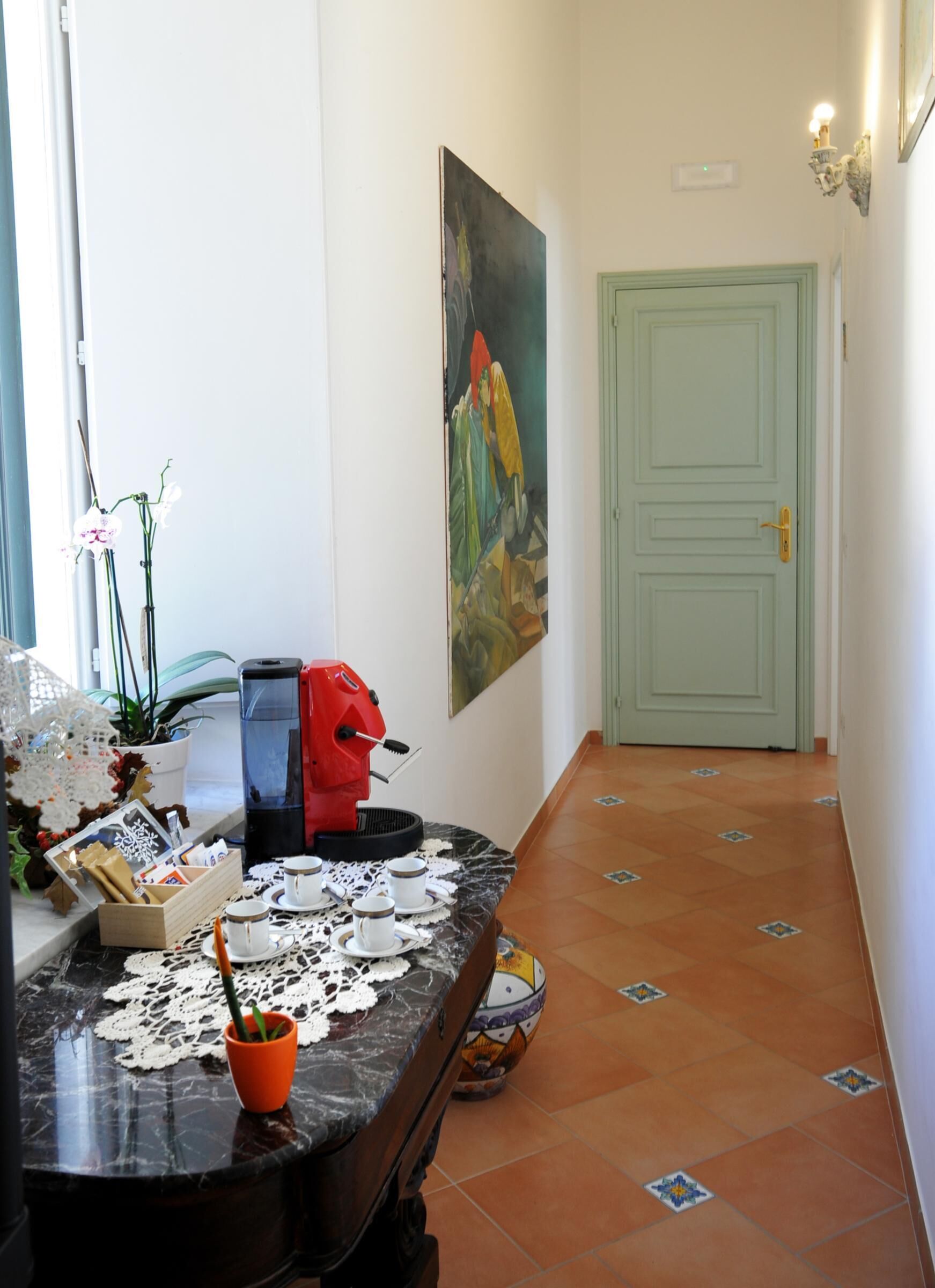 A hallway with a coffee machine, cups, and a table with a lace doily.
