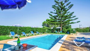 Une piscine entourée de verdure, avec des chaises longues et des parasols, sous un ciel dégagé.