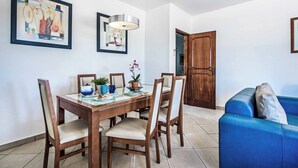 Un coin repas avec une table et des chaises en bois, un canapé bleu et deux œuvres d’art encadrées accrochées au mur.