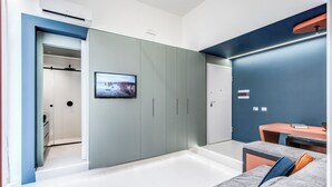 Un dormitorio moderno con un armario gris, un televisor montado en la pared y una pequeña mesa con una silla.