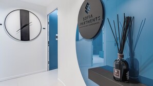 Un interior moderno con un reloj de pared circular, un letrero de Sofia Apartments y un difusor de cañas decorativo.