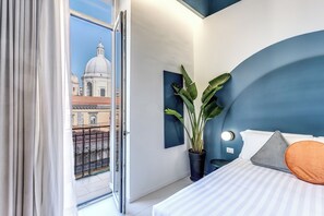 Ein modernes Hotelzimmer mit einem Bett, einer Topfpflanze und Blick auf eine Stadtlandschaft durch eine offene Tür.