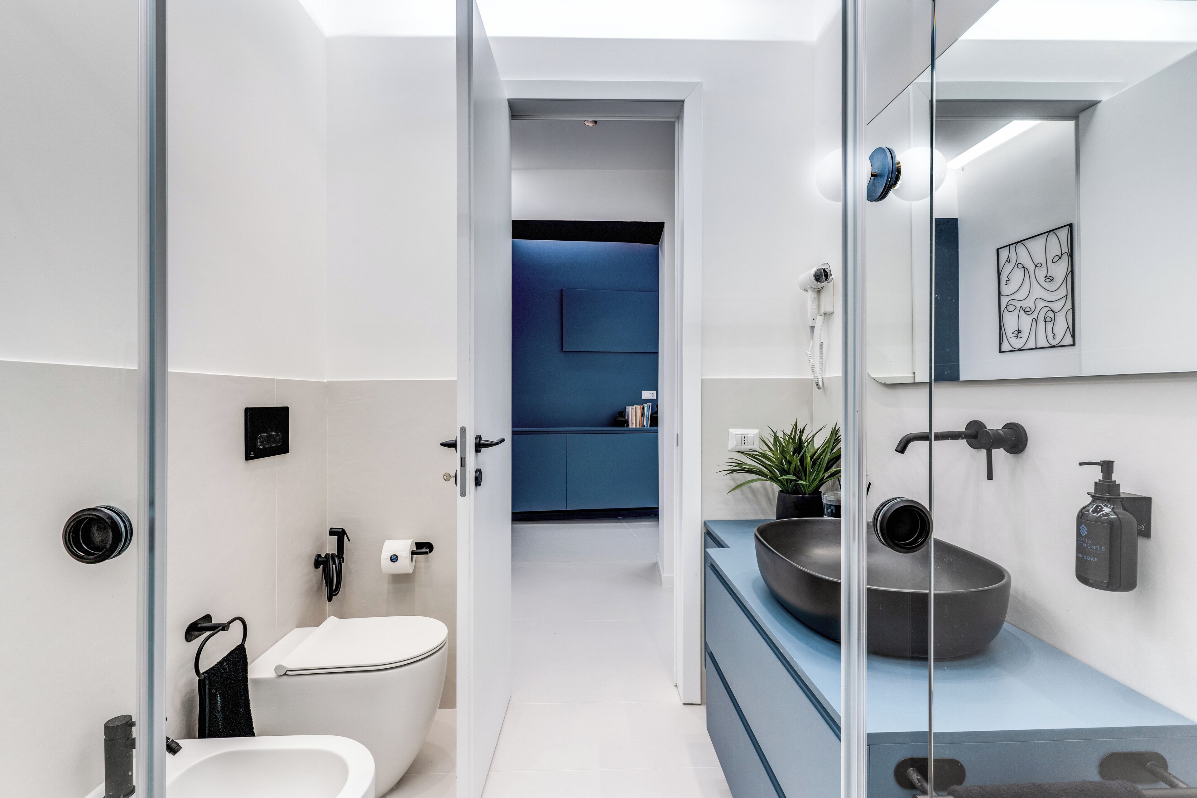 Un bagno moderno con il water bianco, un asciugamano nero, un lavandino capiente e un armadietto blu.