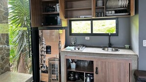 A compact kitchen with a built-in microwave, a sink, and a window overlooking greenery. - Landscape Suite (Cerritos)