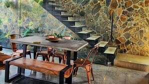 A modern dining area with a stone wall, a wooden table, and copper chairs. - Landscape Suite (Cerritos)