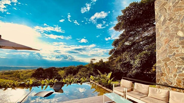 An infinity pool with a wooden deck, outdoor seating, and a stone wall. - Landscape Suite (Cerritos)