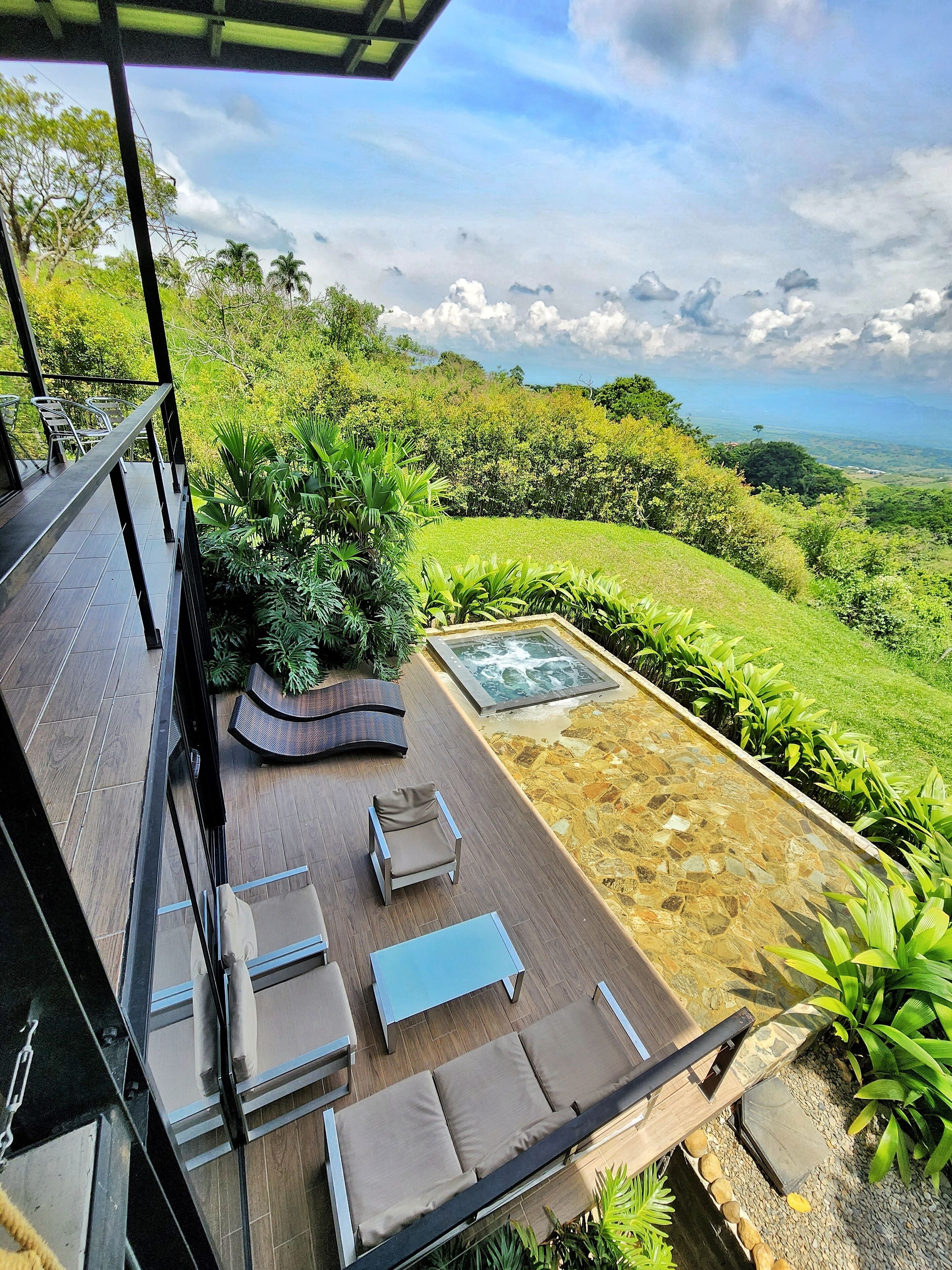 A terrace with outdoor furniture, a hot tub, and a view of a lush landscape.