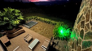 A rooftop patio with outdoor furniture, a hot tub, and a view of a sunset over a mountainous landscape. - Landscape Suite (Cerritos)