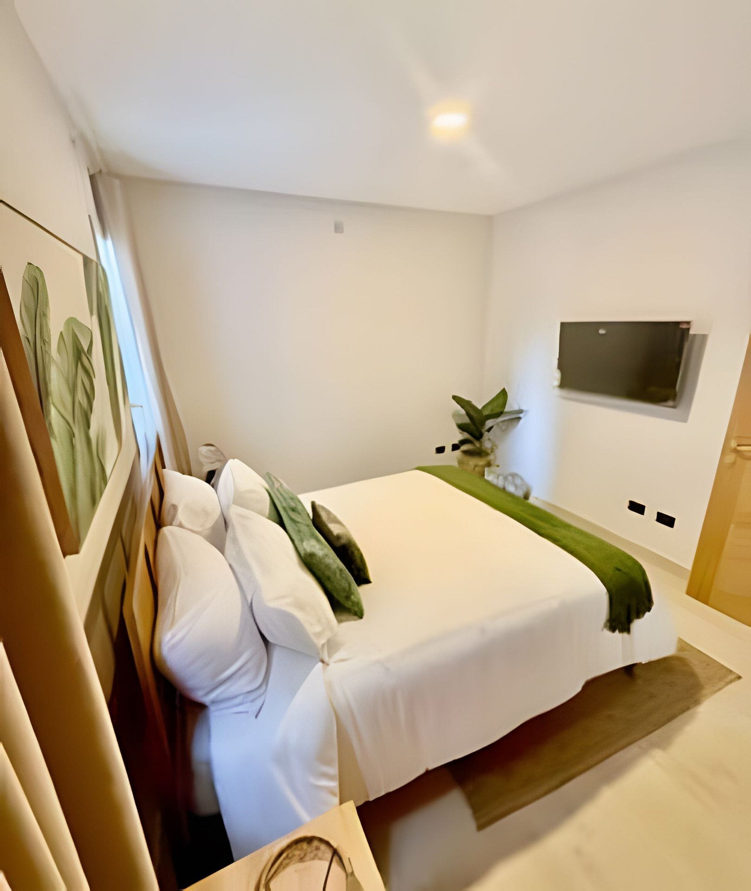 Un dormitori modern amb un llit gran, un televisor de pantalla plana muntat a la paret i una petita planta sobre una estant.