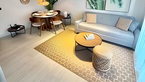 En moderne stue med sofa, sofabord, spisebord og stole. Der er en plante, kunst på væggen og en loftlampe.