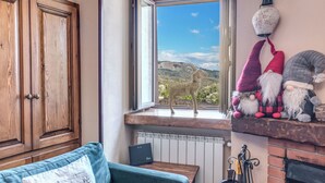 Ein gemütliches Zimmer mit Blick auf eine Berglandschaft durch ein Fenster, einem Holzschrank, einem grünen Sofa und einem Kaminvorsatz mit Dekoration.