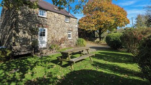 A stone building with a grassy yard, a wooden bench, and a picnic table. - Carthouse Cottage (Clarbeston Road)