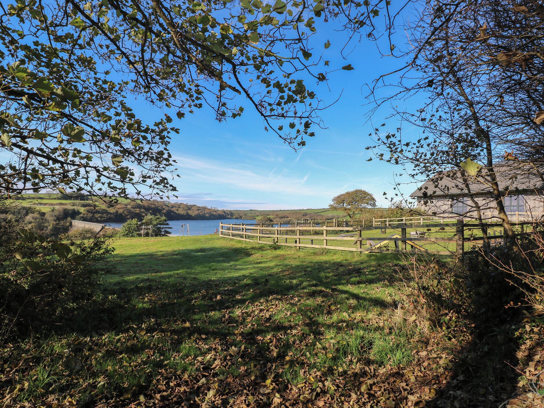 Un paysage rural avec un lac, une clôture en bois et une maison en arrière-plan.