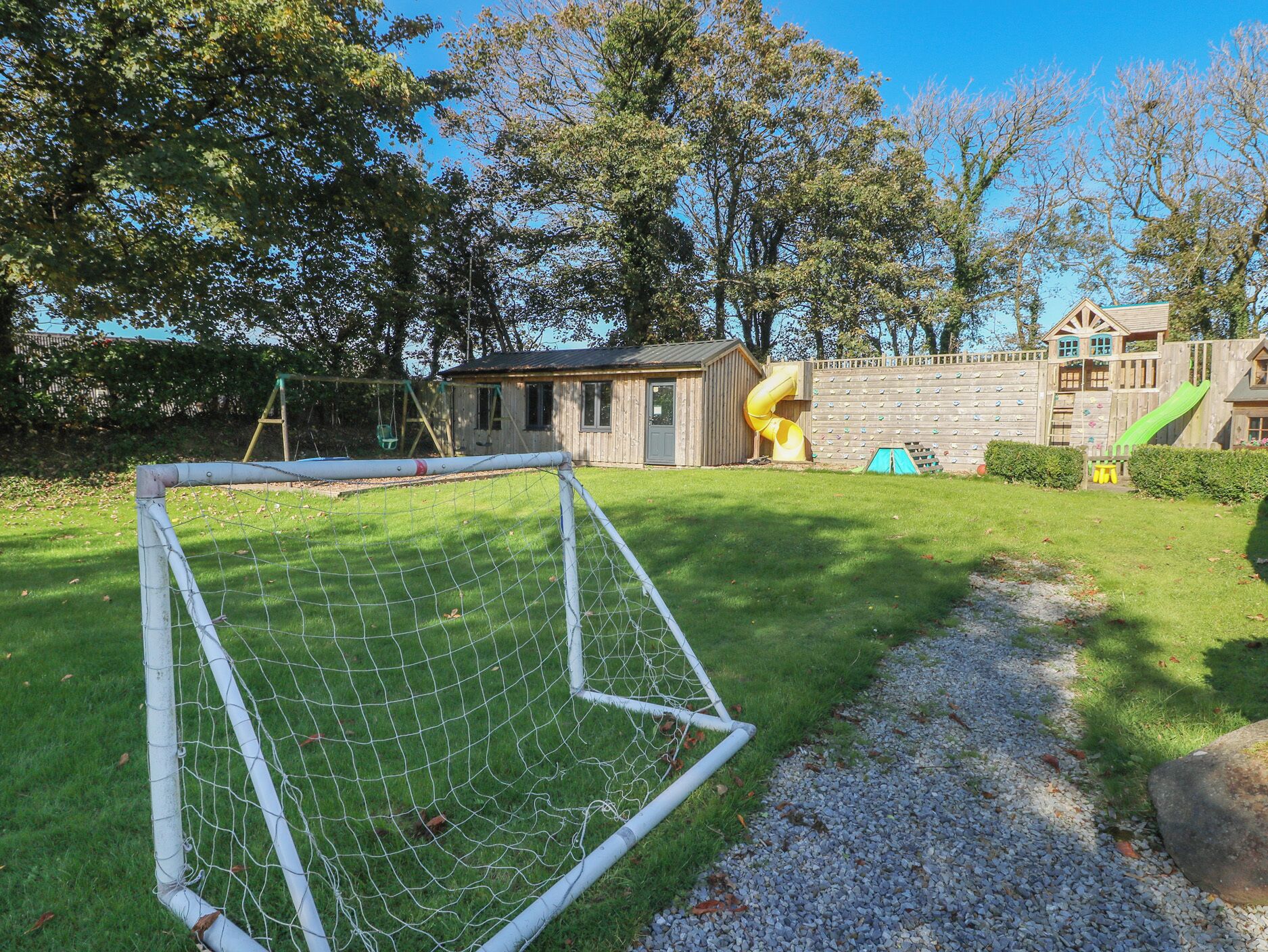 A soccer goal in a grassy area with a playground and wooden structures in the background.