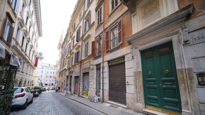 Una strada acciottolata con auto parcheggiate, negozi chiusi e una porta verde sulla destra.