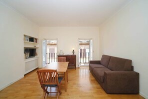 A living room with a brown sofa, a wooden dining table with chairs, and a radiator.