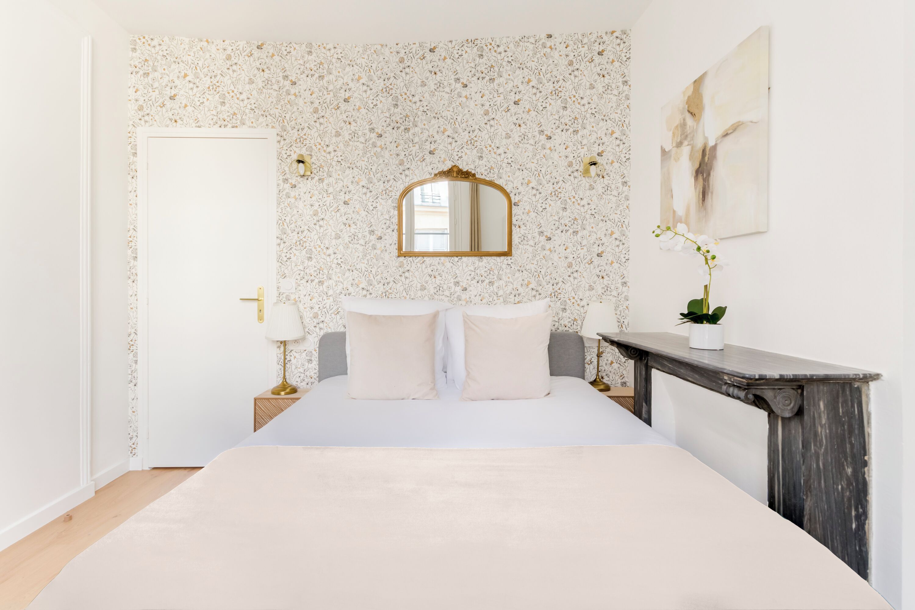 A bedroom with a large bed, a mirror above it, a bedside table with a lamp, and a small potted plant.