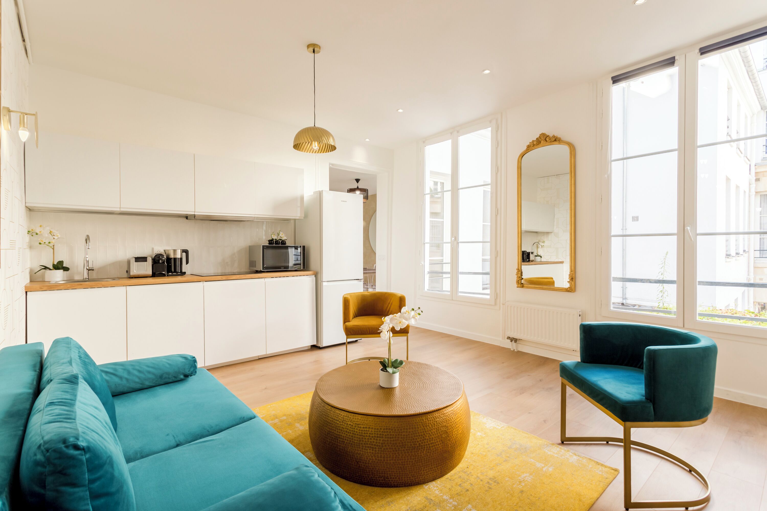 A modern living room with a sofa, a round coffee table, and a chair. There is a kitchen area with cabinets and appliances in the background.
