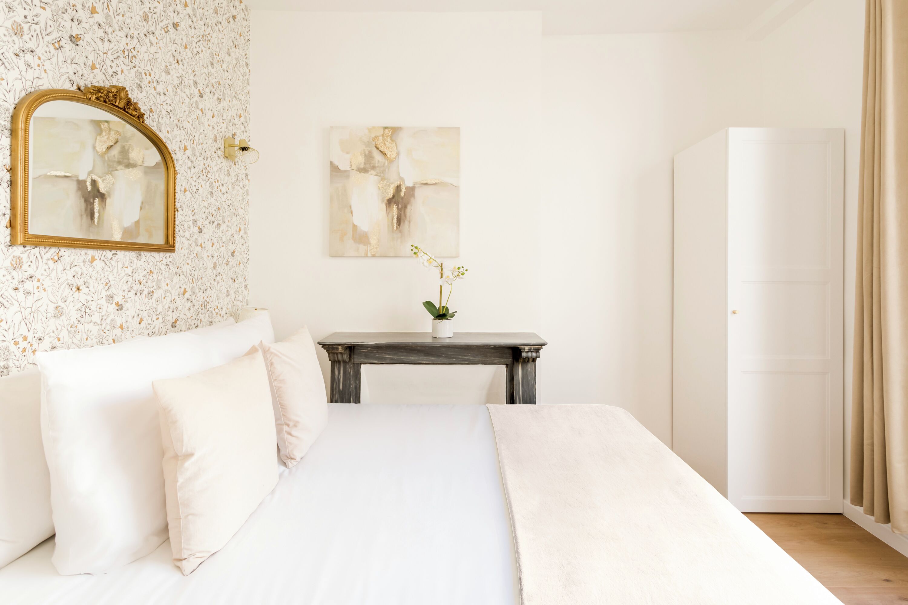 A bedroom with a bed, a nightstand, a mirror, and a door.