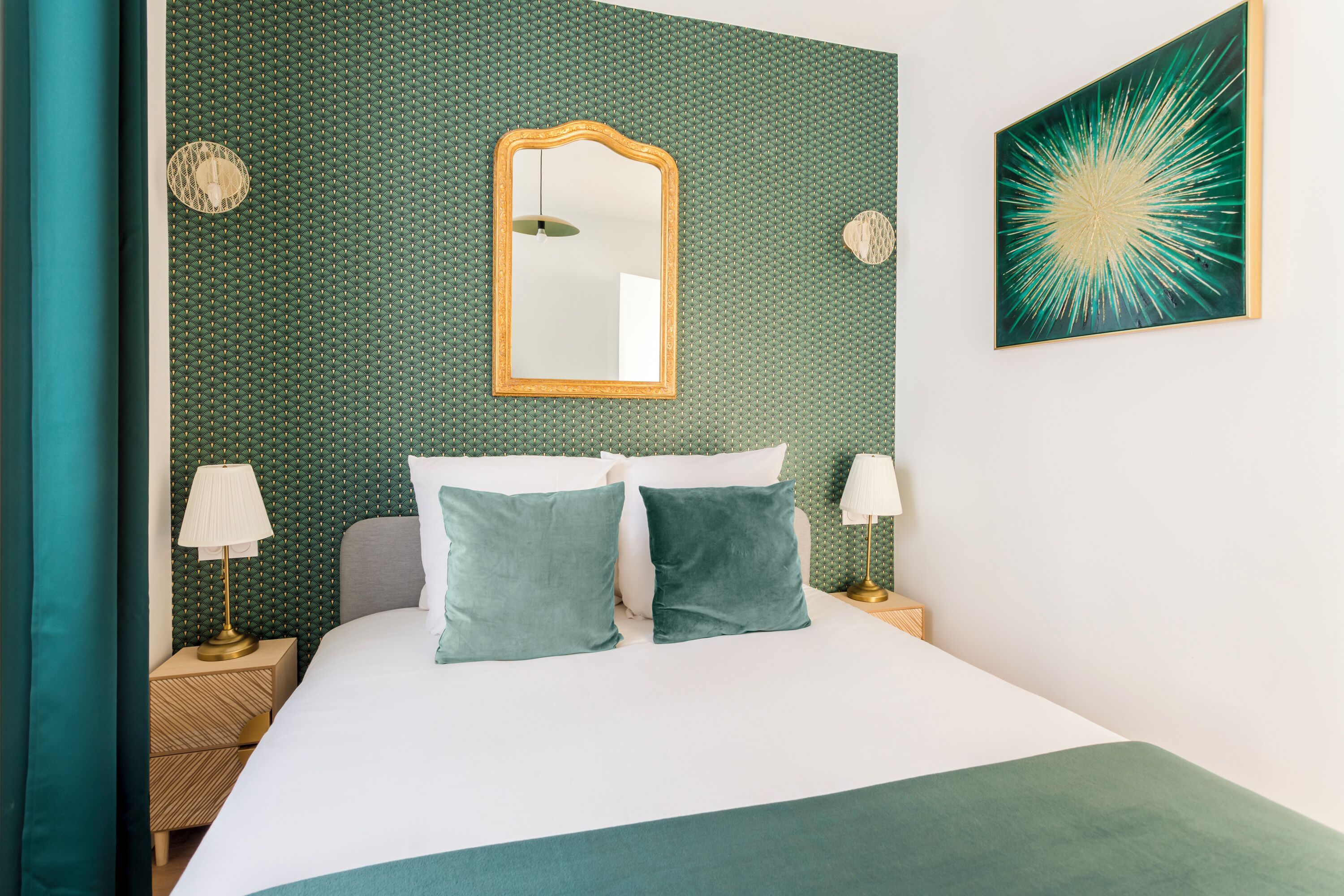 A neatly made bed with two pillows, a nightstand with a lamp, and a wall with a mirror and a painting.