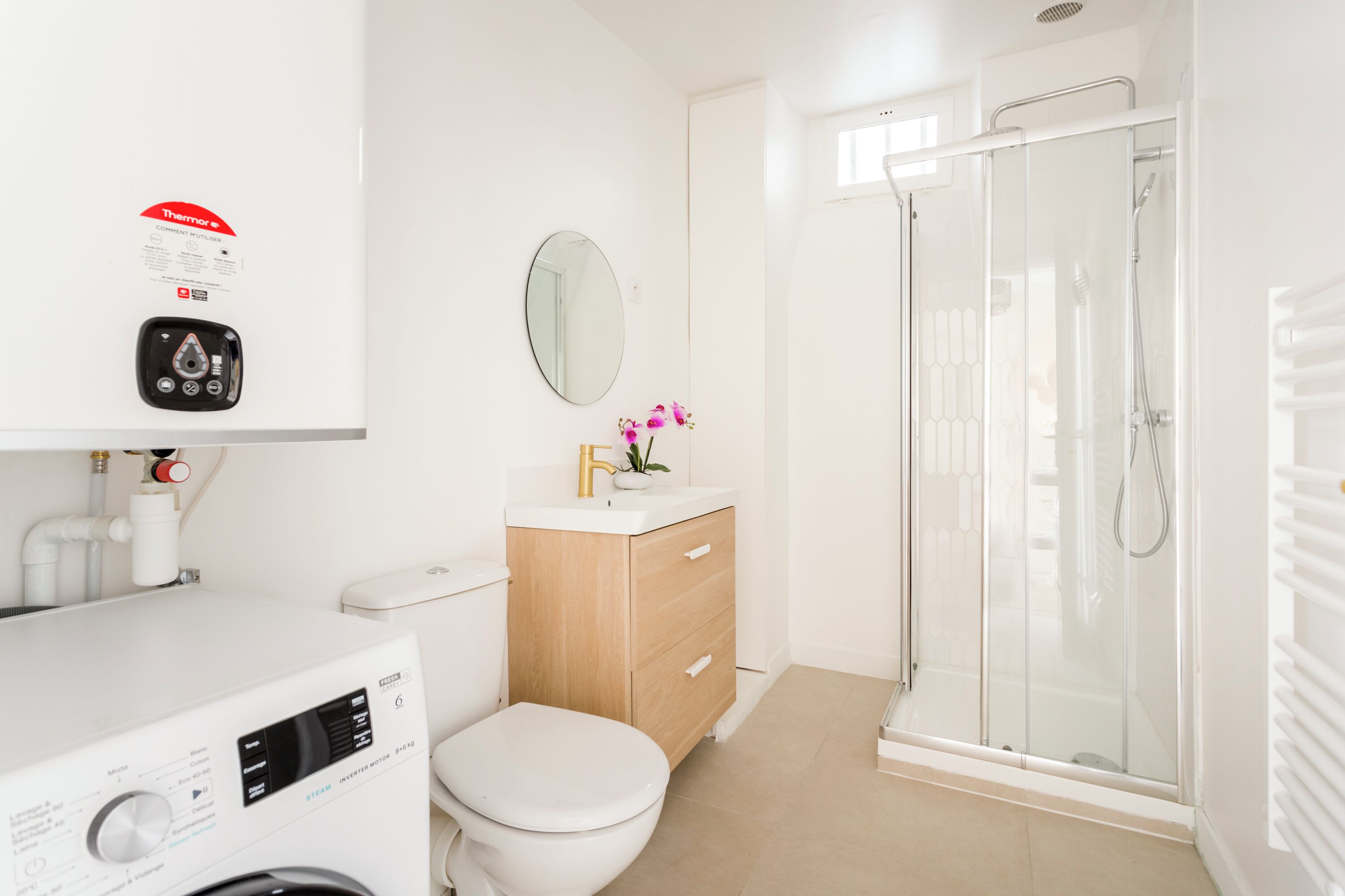 Un baño moderno con inodoro, lavabo con espejo, cabina de ducha y lavadora.